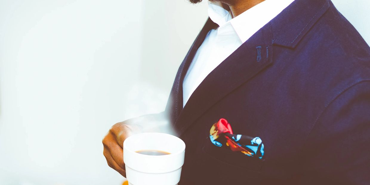 Man in navy blazer holding a steaming cup of coffee.